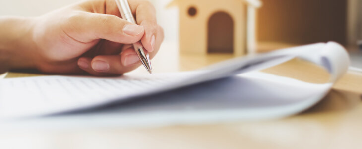 Close up hand of man signing signature loan document to home ownership. Mortgage and real estate property investment